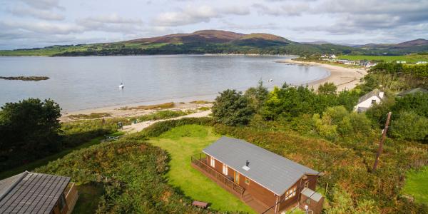 Panoramic view of the sea at Sandgreen with a timber lodge pitch in the foreground